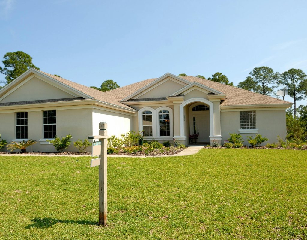 Beautiful suburban house with lush lawn, showcasing a for sale sign under a clear blue sky.