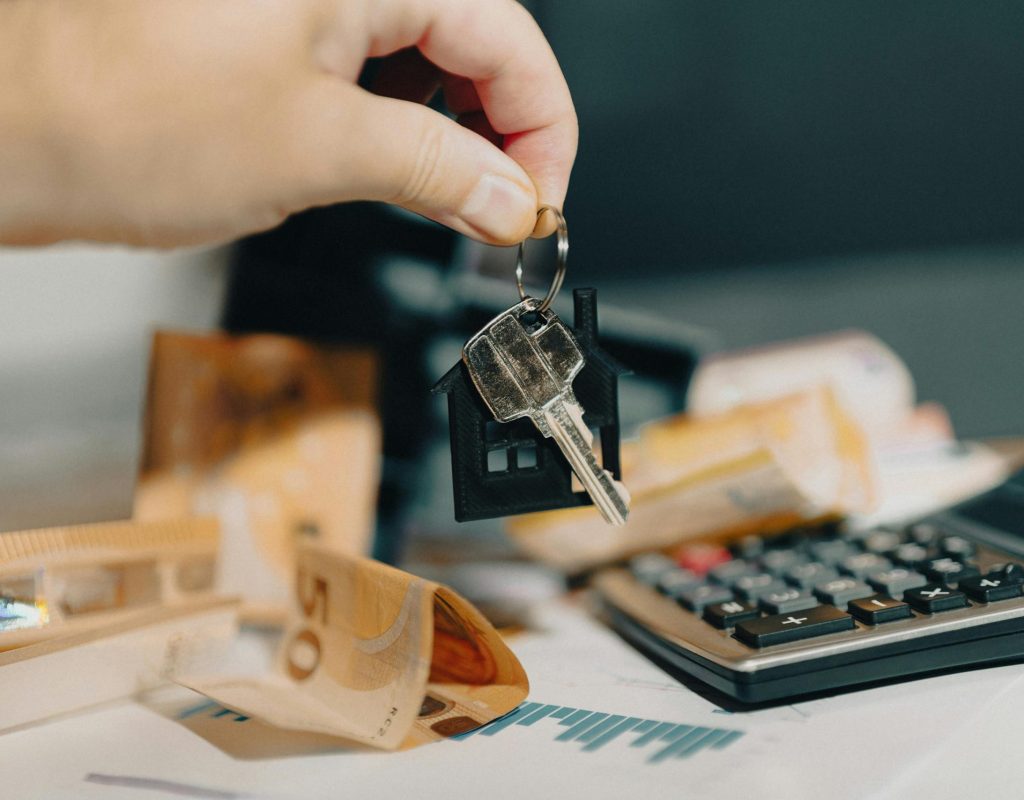 Close-up of a hand holding keys over euros and calculator, symbolizing real estate purchase.