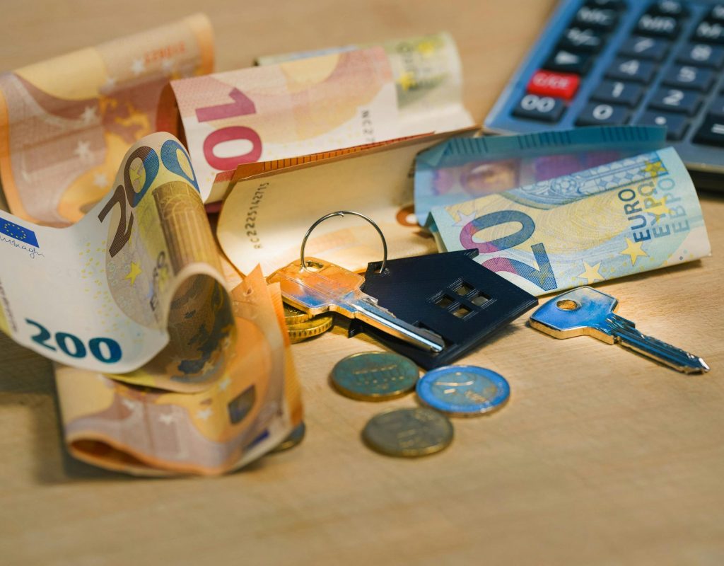 Euro banknotes and coins with house keys on a table symbolize finance and real estate.