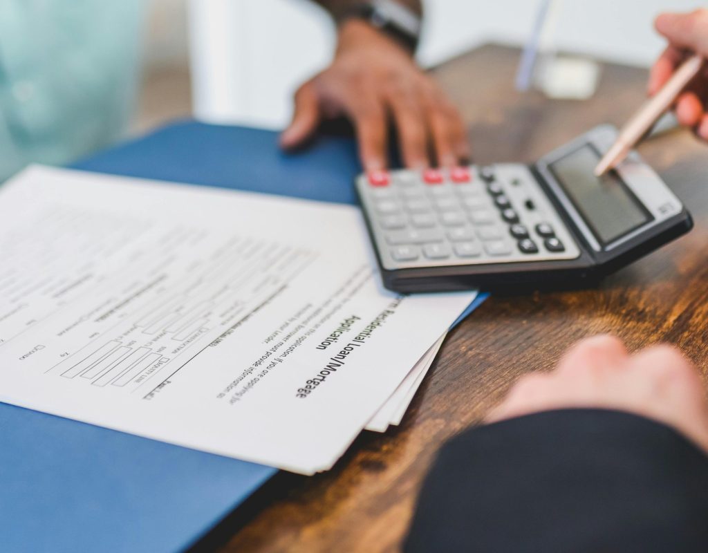 Hands using a calculator with real estate documents on a desk, indicating a financial transaction or meeting.