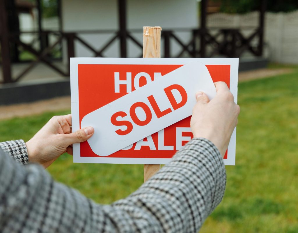 Close-up of hands placing a sold sticker on a real estate sign outside a house.